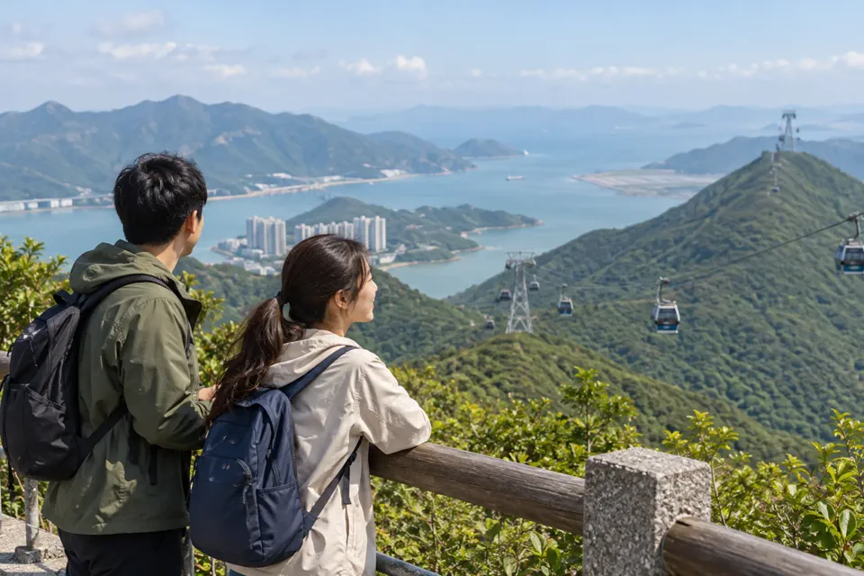 緑豊かなランタオ島の山と海を眺め、ロープウェイの見える展望地に立つ旅行者