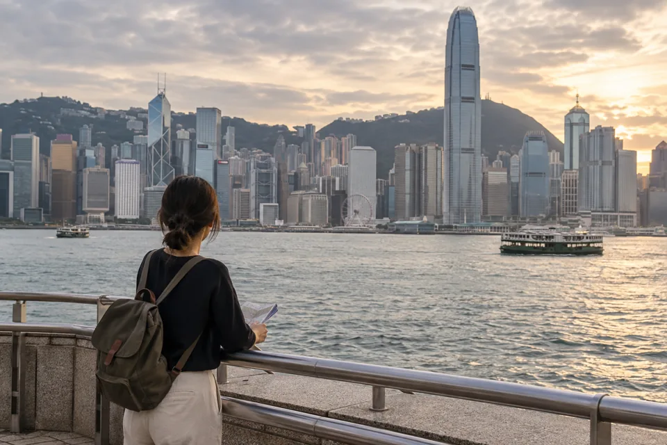ビクトリアハーバー越しに香港島の高層ビル群を眺めながら、地図を手に旅程を考える旅行者