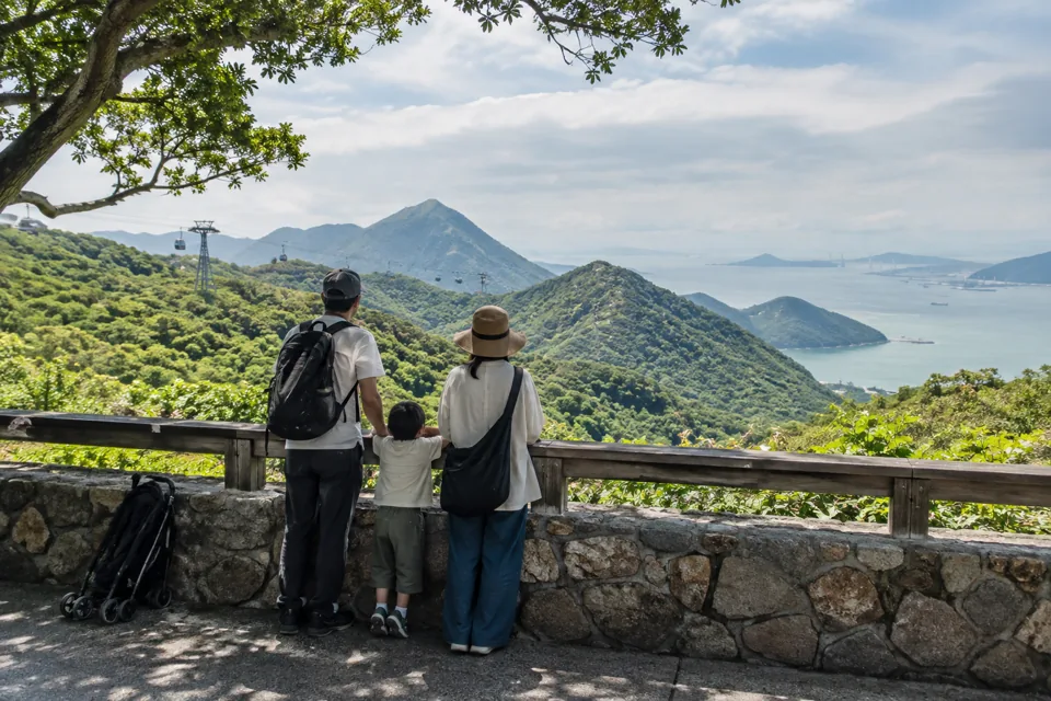 緑の山と海を望むランタオ島の展望地で、子ども連れの旅行者が景色を眺めている様子