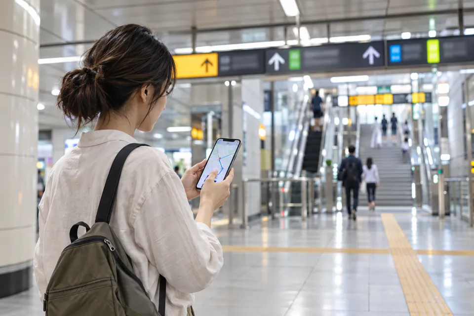 地下鉄のコンコースでスマートフォンの地図と出口方向を確認する旅行者