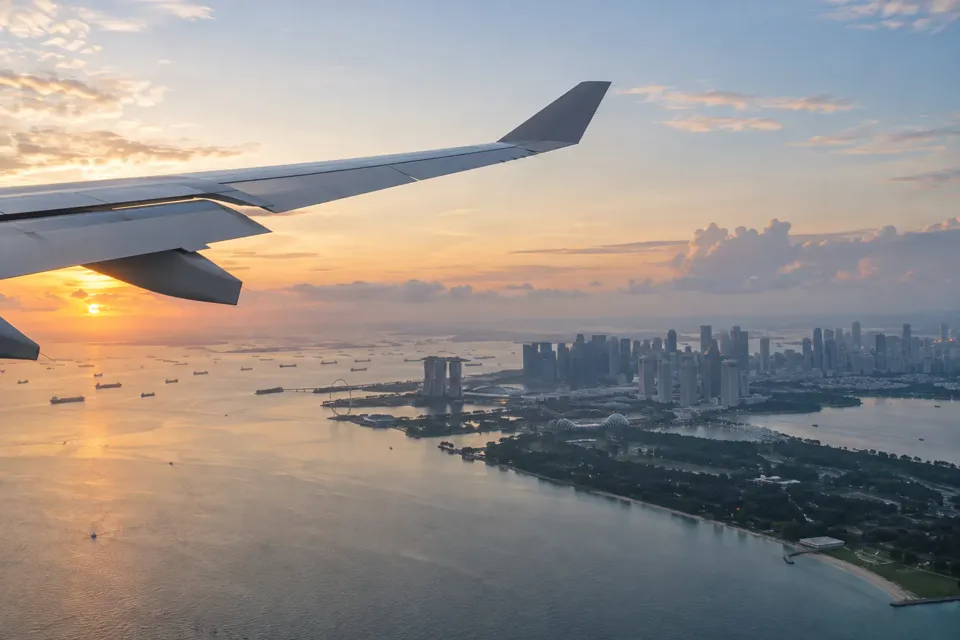 朝焼けの空からシンガポールの海岸と市街地を見下ろす飛行機の窓からの景色